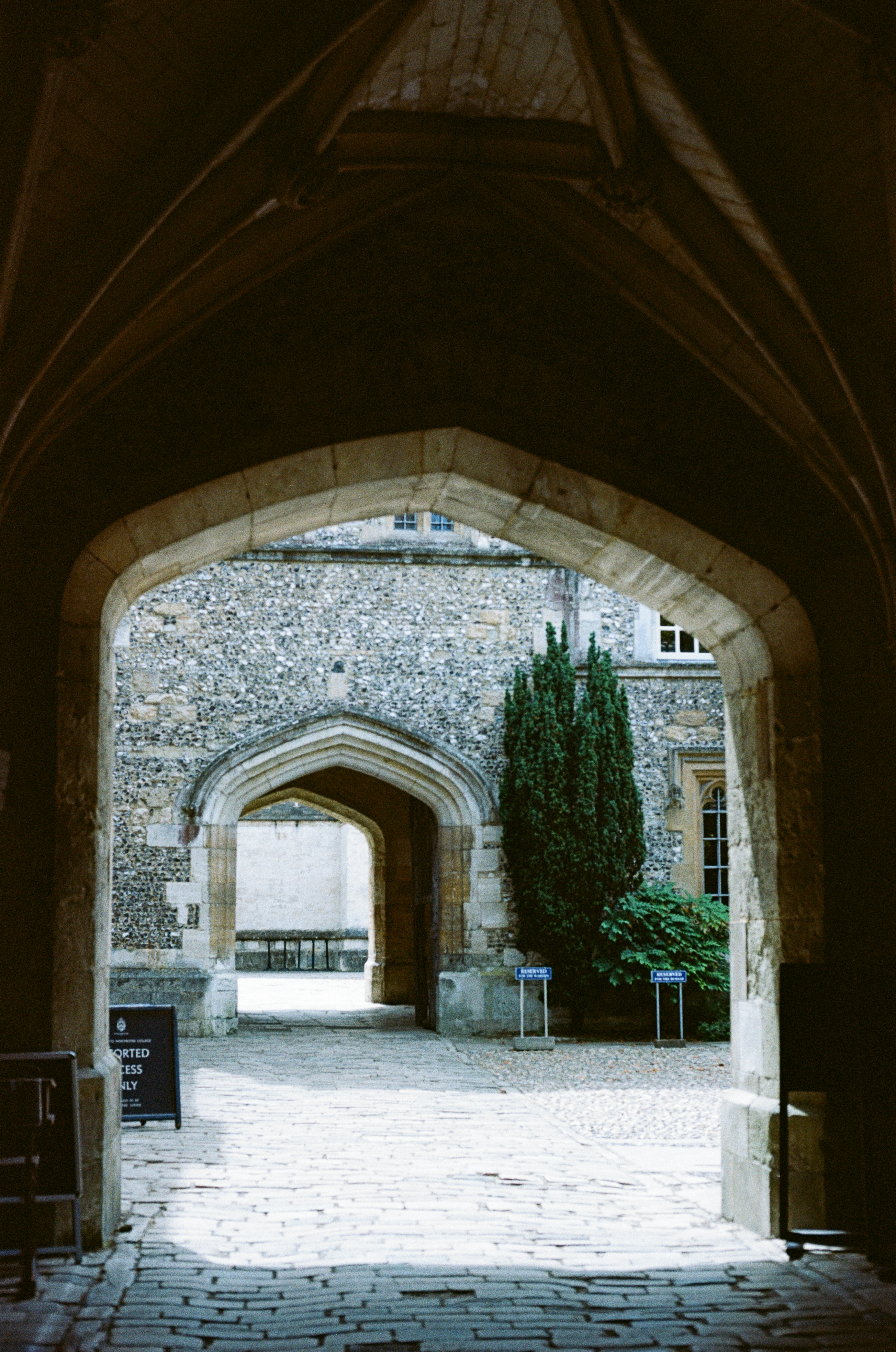 An open Gothic stone archway looking through to a sunlit courtyard and a second open arch